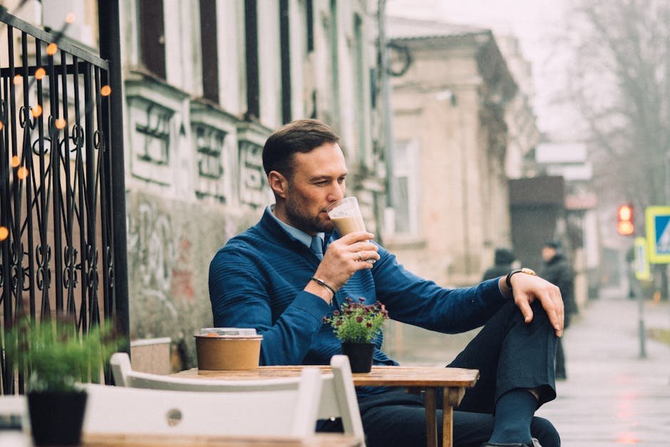 Young man sipping coffee at an outdoor cafe, enjoying a relaxing moment in a lively urban setting.