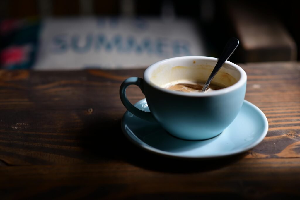 pexels-photo-33207663-33207663 A blue coffee cup with a spoon sits on a wooden table, conveying a cozy summer ambiance.